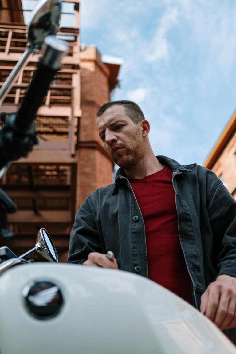 A mechanic focuses on maintaining a motorbike outside a brick building.